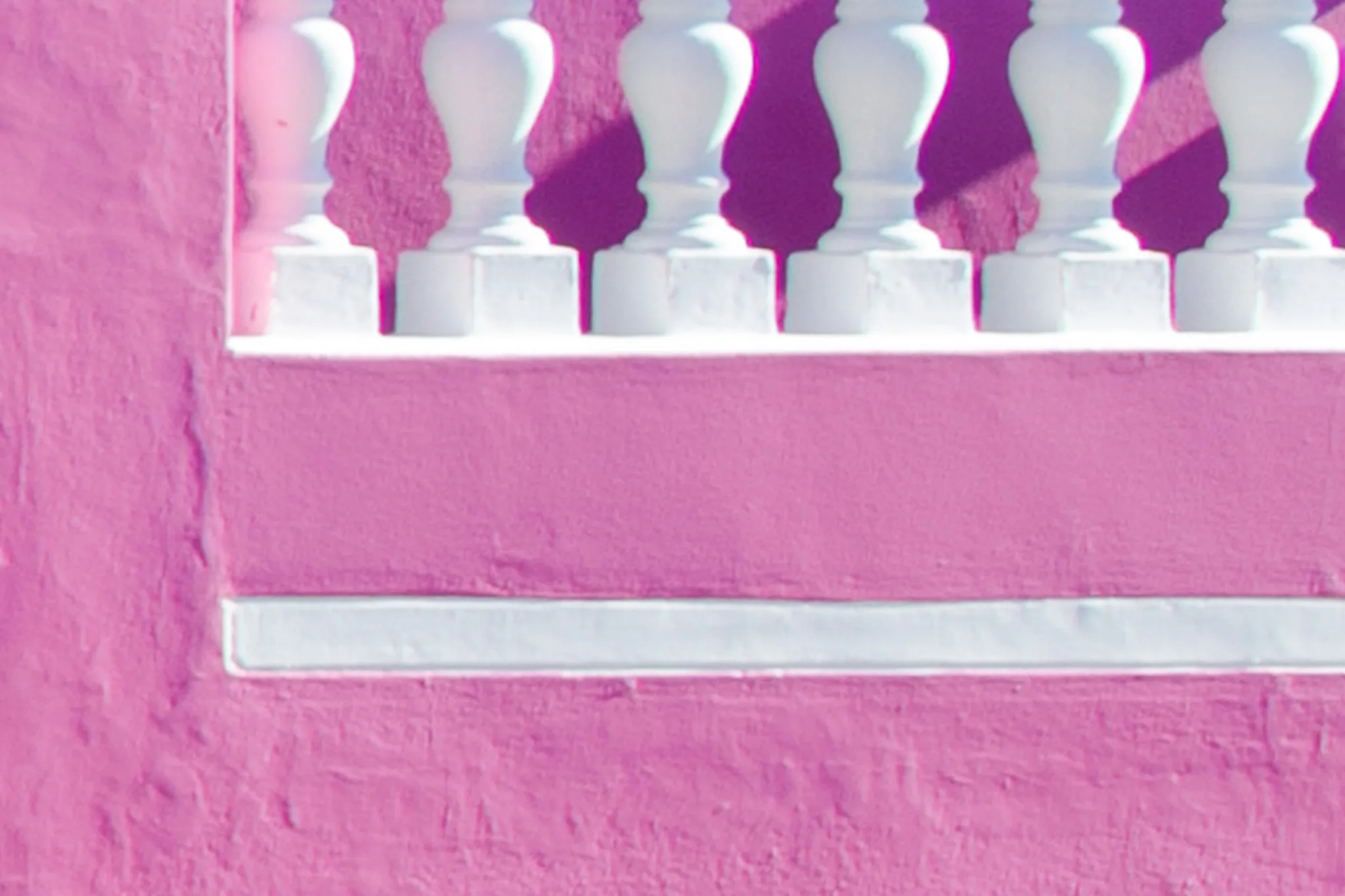 A white balustrade on a bright pink wall with sharp shadows. A white balustrade on a bright pink wall with sharp shadows.