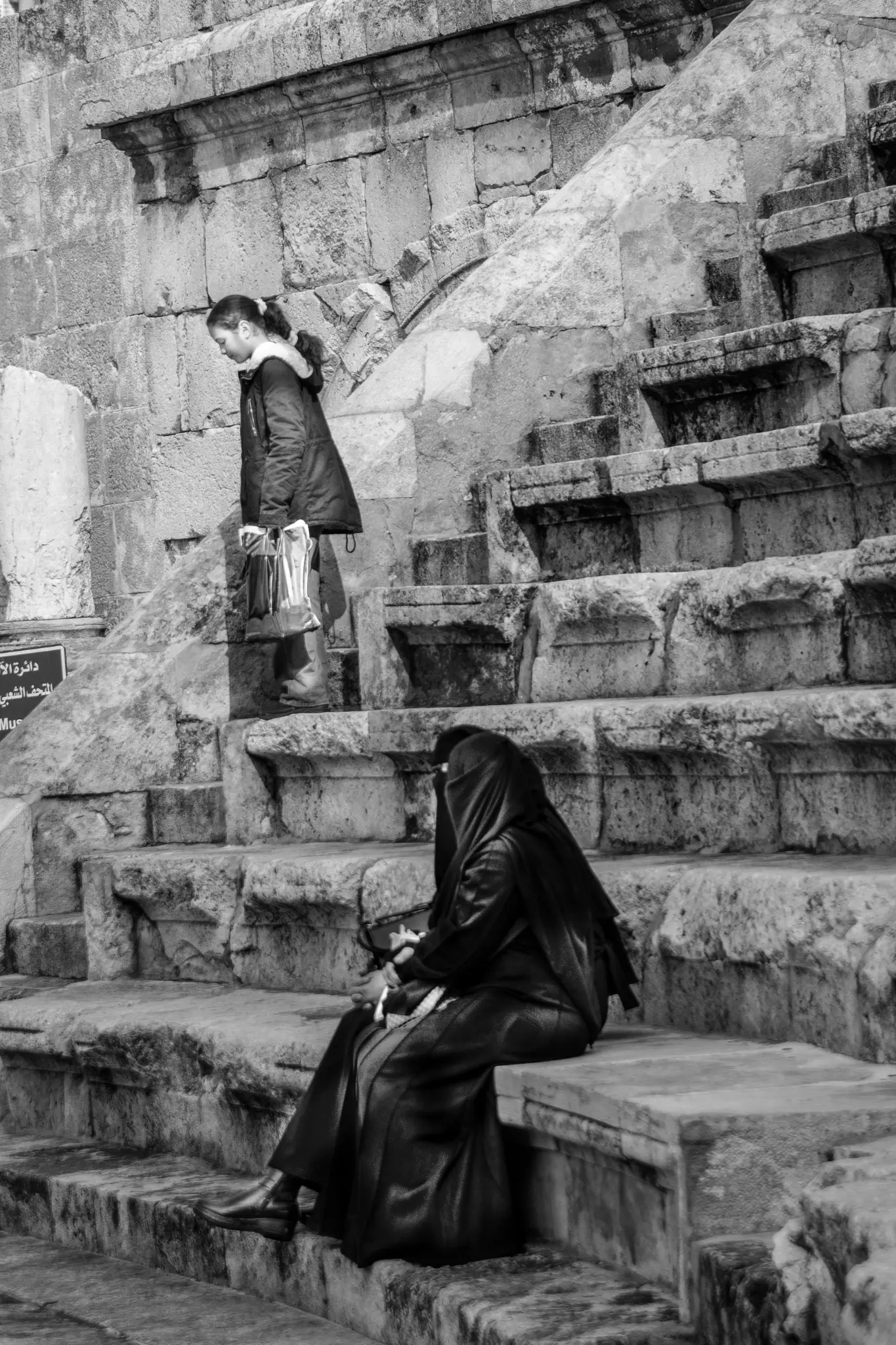 A woman sits on stone terraces as a girl walks down the steps.