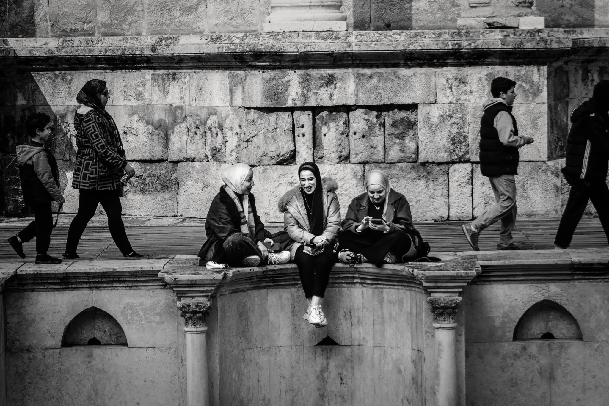 Three girls smile while sitting on the stone terraces of Amman’s Roman Theatre.