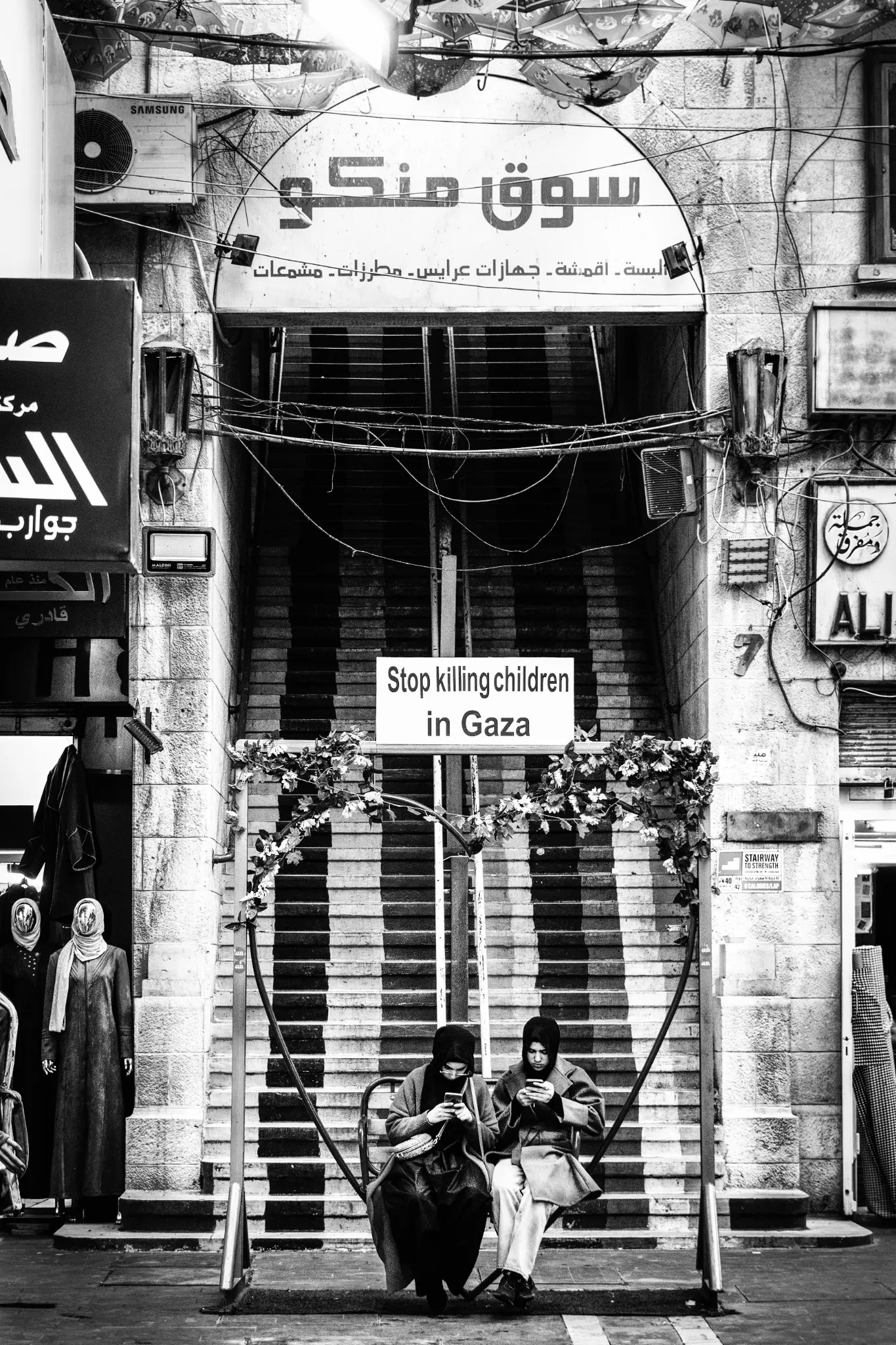 Two young women sit beneath a sign reading “Stop killing children in Gaza”.