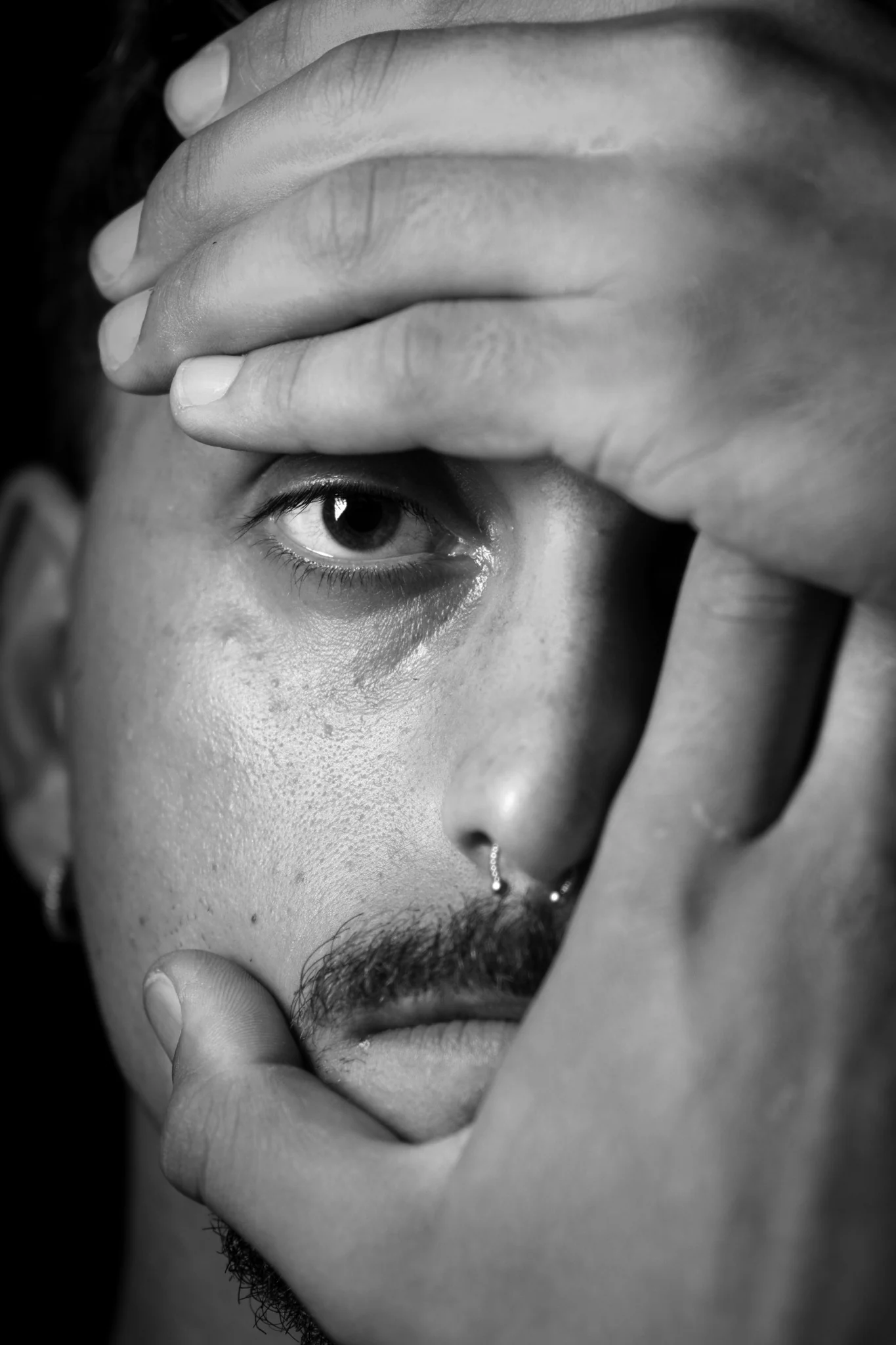 Ritratto in bianco e nero di un uomo con un occhio incorniciato dalle mani.