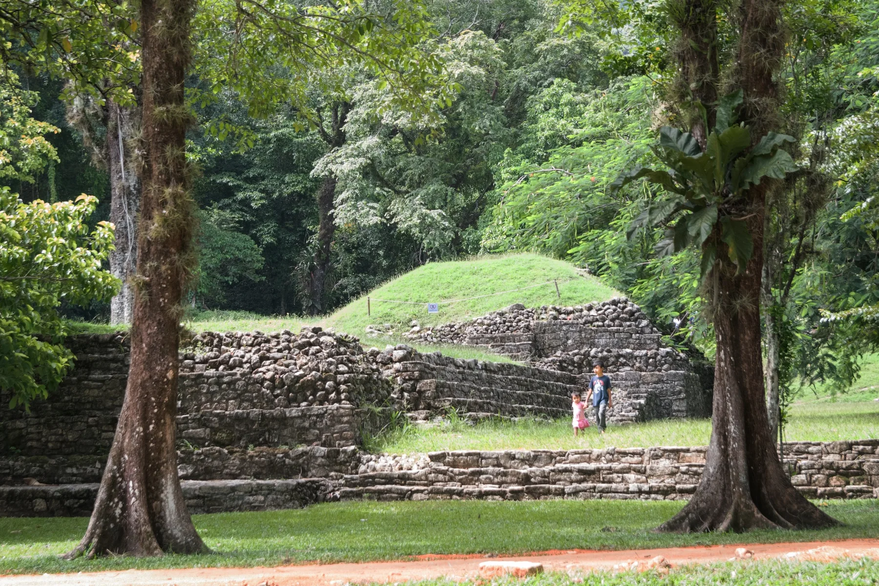 Ruins surrounded by greenery with two children walking nearby.