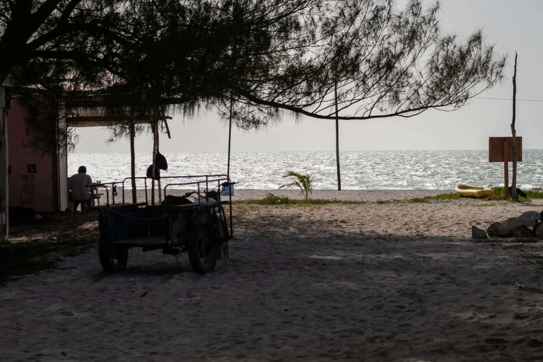 A backlit beach with a figure seated beneath a shelter.
